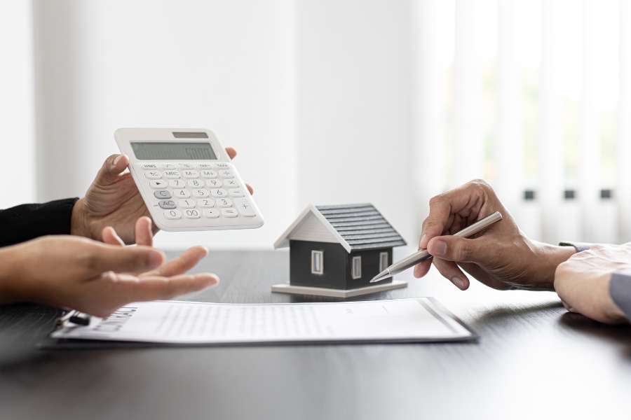 Two people discussing financial documents and using a calculator near a house model, representing title insurance.
