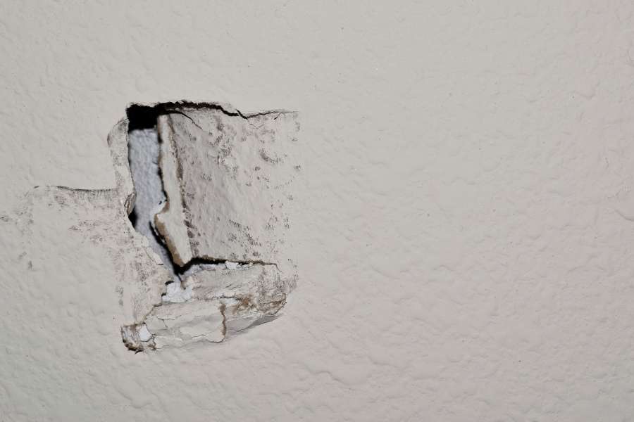 A close-up view of a damaged drywall hole in a textured white wall.