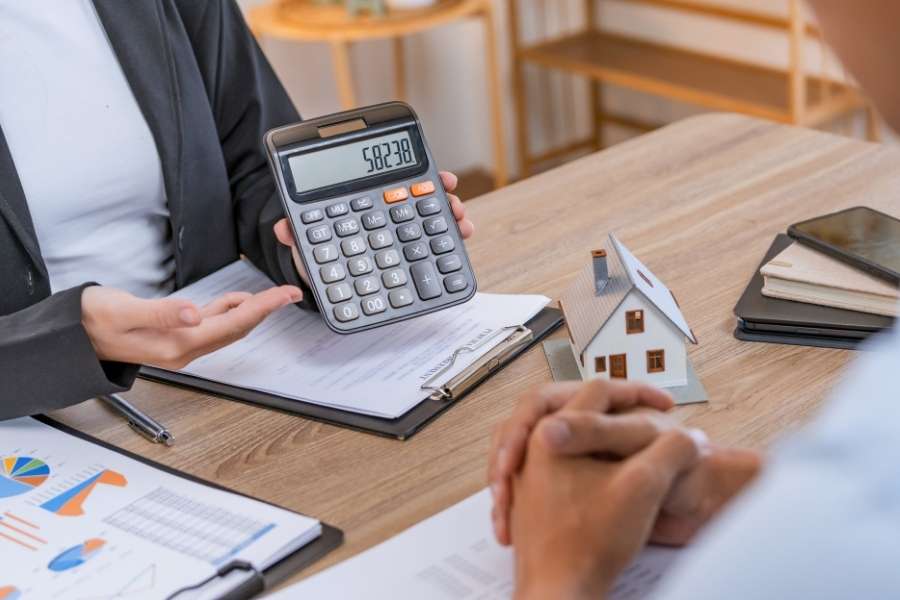 A person showing a calculator with a model house to prove a neighborhood is a smart investment.