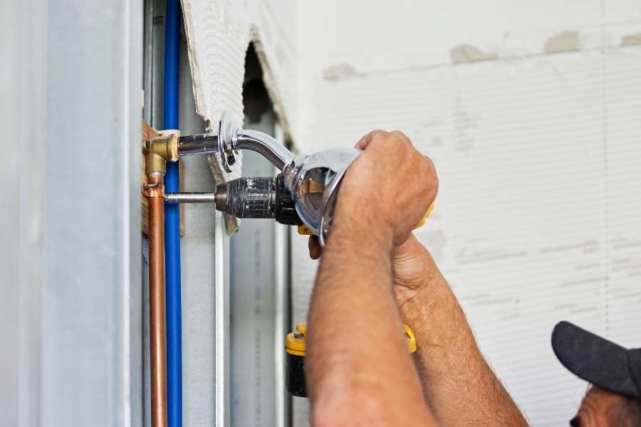 A worker using a power drill to install fixtures for common bathroom plumbing.