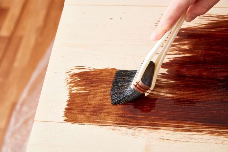A person applying dark stain with a brush, addressing wood finishing turning out blotchy.